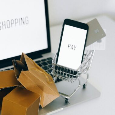 A miniature shopping cart holds a smartphone and credit card on a laptop, symbolizing online shopping.