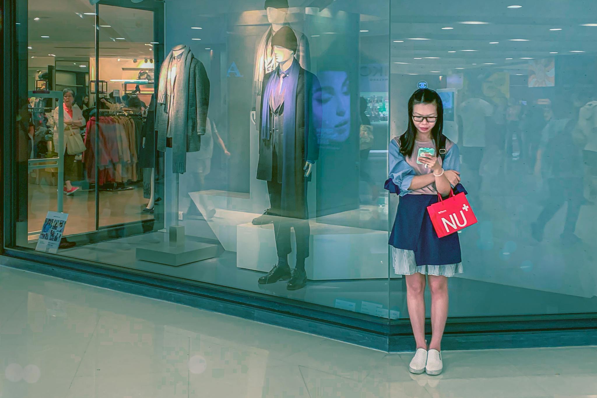 Asian woman using smartphone outside a clothing store in Kowloon mall, Hong Kong.