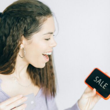 Happy woman holding a smartphone and sale sign, showcasing excitement for shopping deals.
